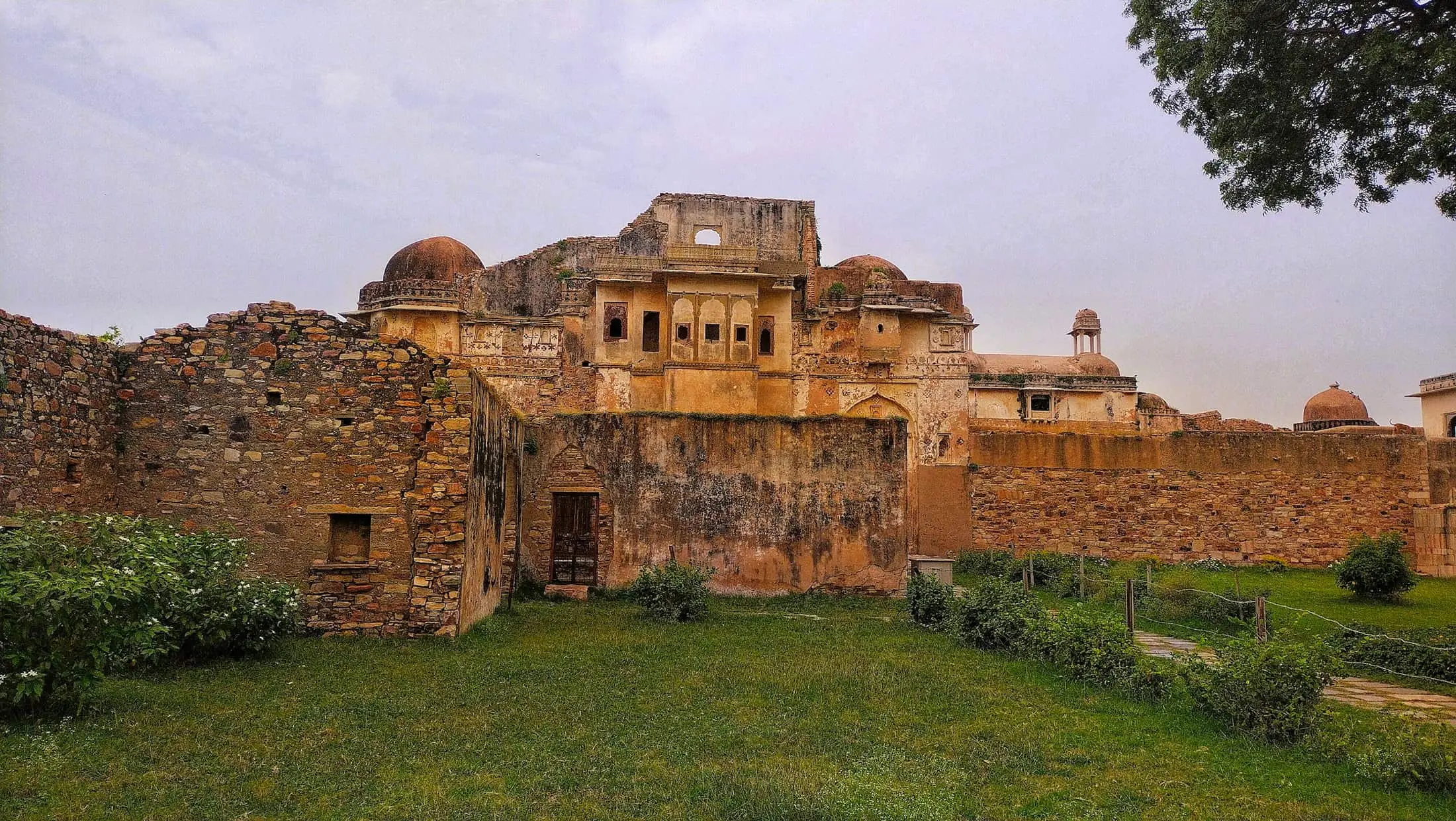 Weathered stone palace ruins with domed pavilions above a green lawn at Chittorgarh