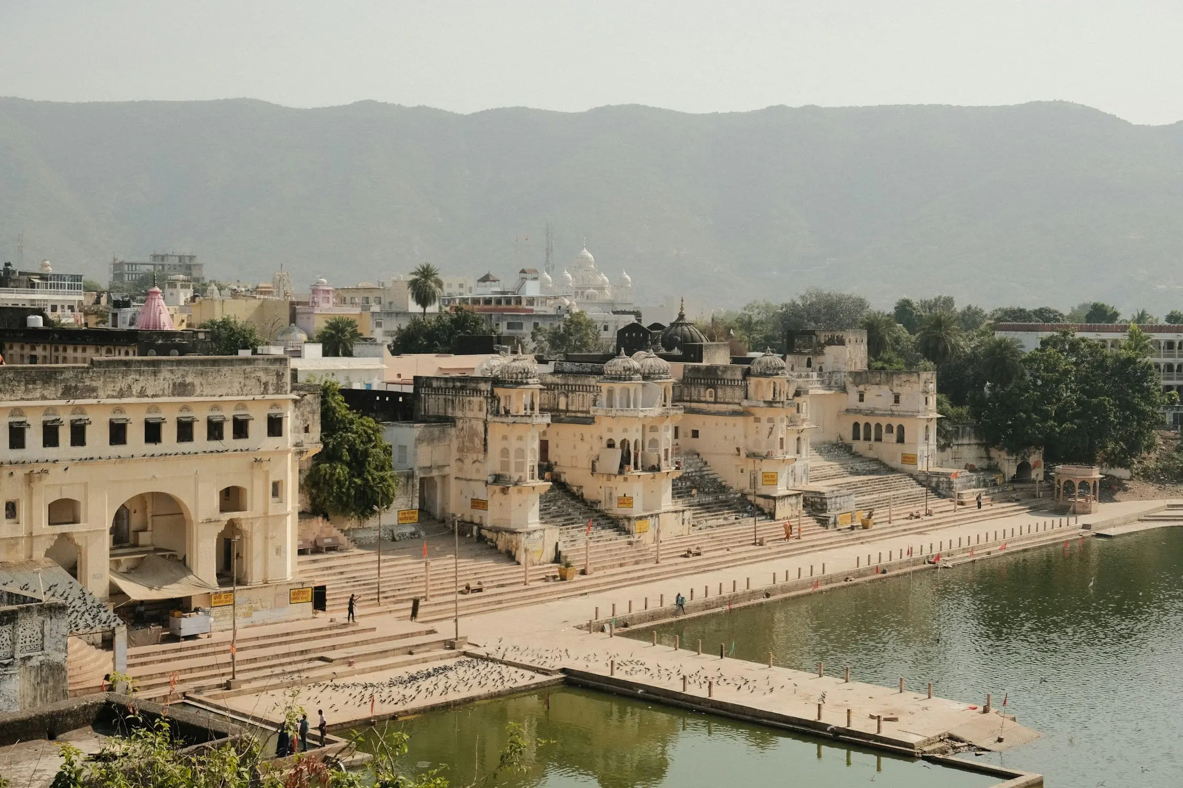 Stone ghats and pavilions lining Pushkar Lake, with hills in the distance