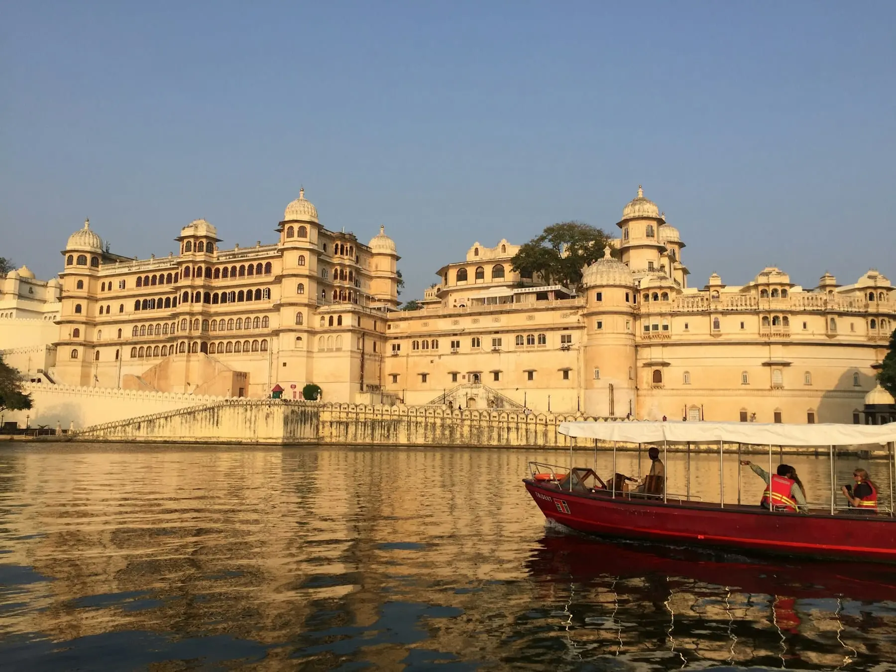 A red boat with passengers on Lake Pichola below the City Palace in warm afternoon light